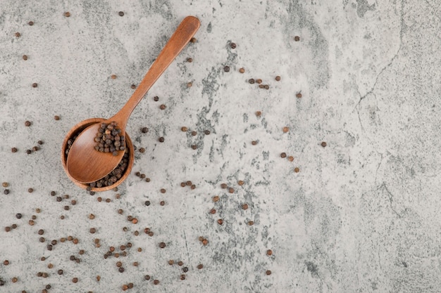 Small wooden bowl of pepper grains on marble background