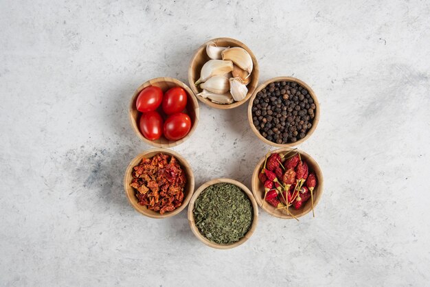 Small wooden bowls of spices and tomatoes on marble background.