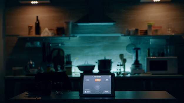 Smart application on tablet placed on kitchen desk in empty house automation system turning on the l...