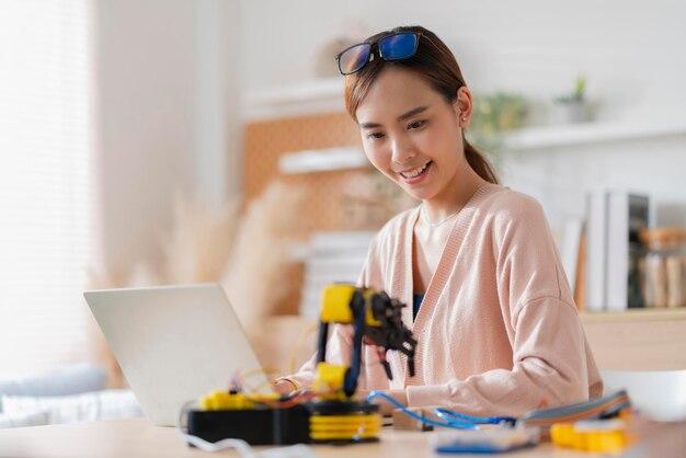 Smart asian female programer learning robot arm ai coding electronic board cable in STEM STEAM she try to testing her autonomous robotic arm with sensors via Arduino platform at home