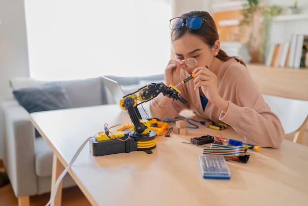 Smart asian female programer learning robot arm ai coding electronic board cable in STEM STEAM she try to testing her autonomous robotic arm with sensors via Arduino platform at home