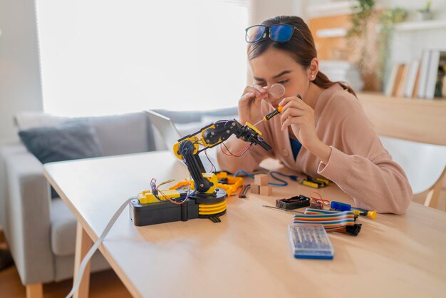 STEMSTEAMでロボットアームaiコーディング電子ボードケーブルを学習するスマートなアジアの女性プログラマー彼女は自宅のArduinoプラットフォームを介してセンサー付きの自律型ロボットアームをテストしようとしています