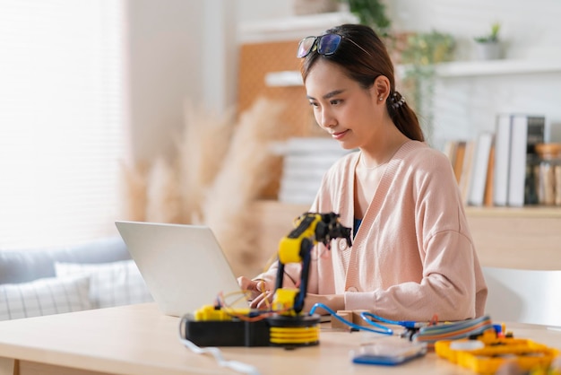 Smart asian female programer learning robot arm ai coding electronic board cable in STEM STEAM she try to testing her autonomous robotic arm with sensors via Arduino platform at home