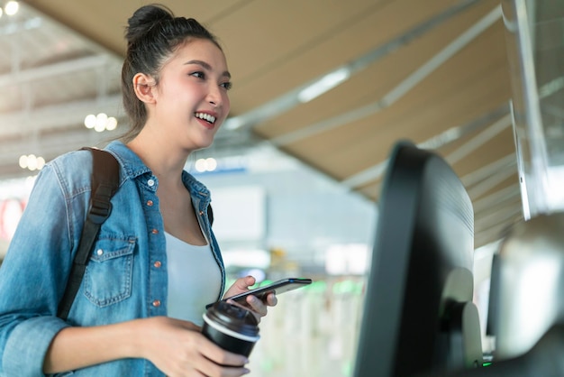 Умная азиатская женщина-путешественница самостоятельно регистрируется на рейс на транспорте у ворот, сканирует устройство монитора на стойке регистрации в аэропорту, встречная концепция умных технологий, идеи путешествий в терминале