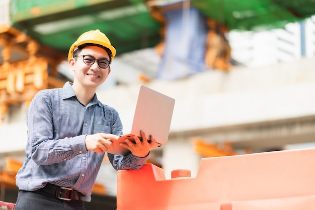 Controllo di costruzione del sito del laptop della tenuta della mano dell'ingegnere civile professionista maschio asiatico astuto con priorità bassa dell'edificio e dell'infrastruttura