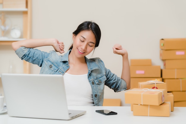 Smart Asian young entrepreneur business woman owner of SME working and relax raise arm up and close eye in front of laptop computer on desk at home. 