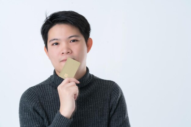 Умный привлекательный азиатский бизнесмен держит кредитную карту в руках, думает и концентрируется на белом фоне