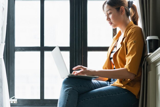 smart attractive asian female creative woman happiness working with laptop casual dress sit next to window with light glow freelance work from home ideas concept