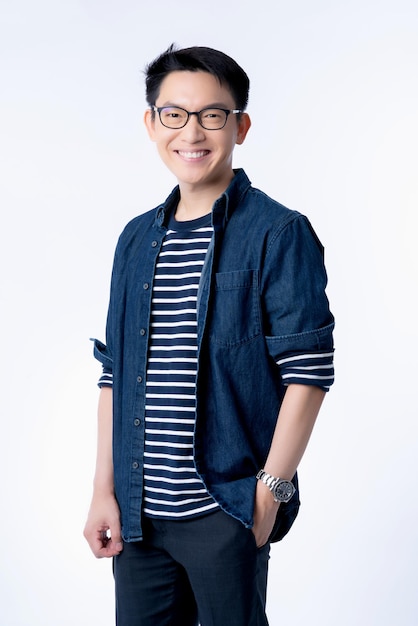 スマートな魅力的なアジアのメガネ男性立って、新鮮さと楽しいカジュアルな青いシャツの肖像画の白い背景で笑顔
