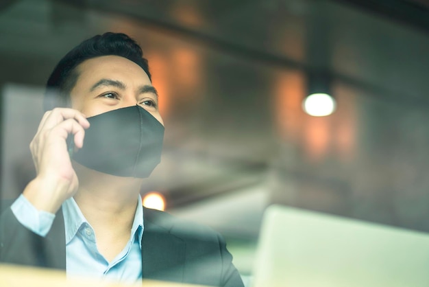 Smart attractive asian male businessman wearing face mask virus protecting working with smartphone in cafe new normal working lifestyle business concept