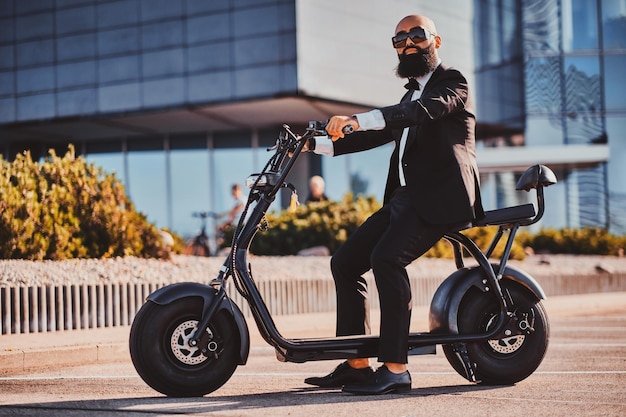 Smart attractive businessman is sitting on his electro scooter while posing for photographer.