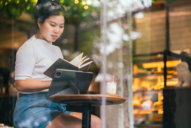 Smart attraente positivo asiatico nomade digitale femmina che indossa un panno casual lavoro remoto nuovo stile di vita normale uso manuale tablet teleconferenza onlive videochiamata riunione remota al coffeeshop cafe