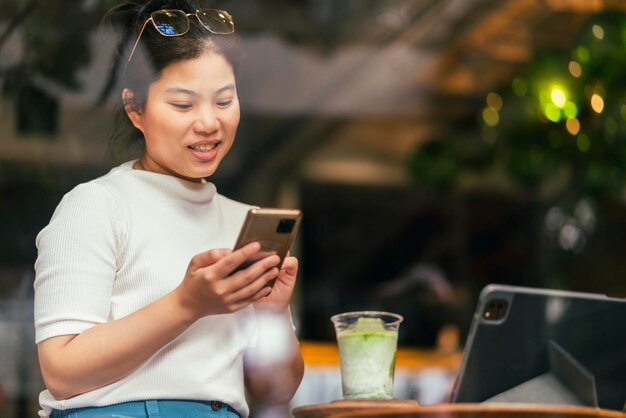 캐주얼 천으로 작업하는 스마트하고 긍정적인 아시아 디지털 유목민 여성은 커피숍 카페에서 원격으로 태블릿 원격 회의 온라인 화상 통화 회의를 사용합니다.