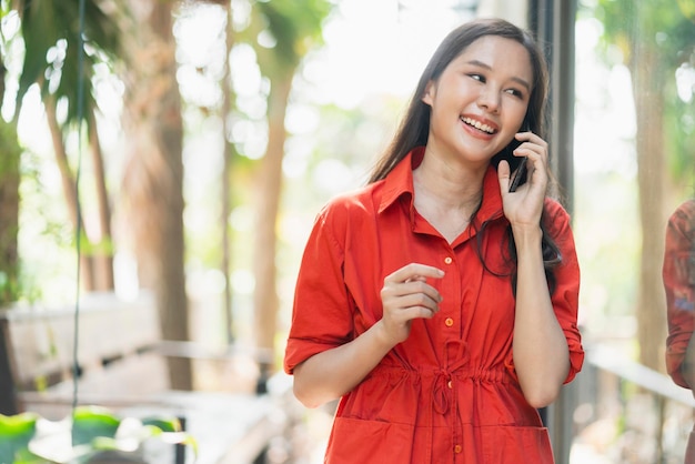 Умная красивая привлекательная азиатская женщина длинные волосы улыбка рука держит смартфон связь социальная связь идеи концепция размытие боке сад фон азия женщина улыбается прогулка возле большого окна кафе