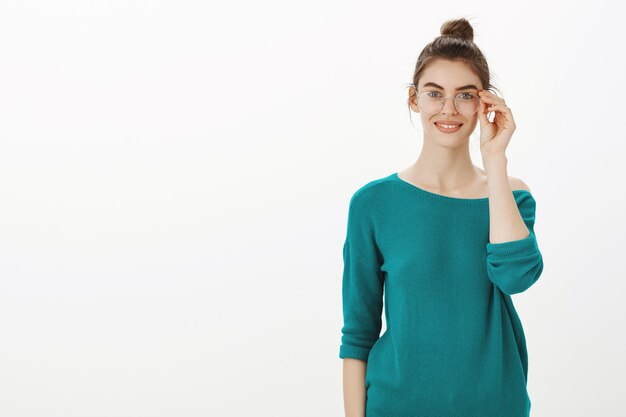 Smart and creative young woman in glasses smiling pleased over white wall