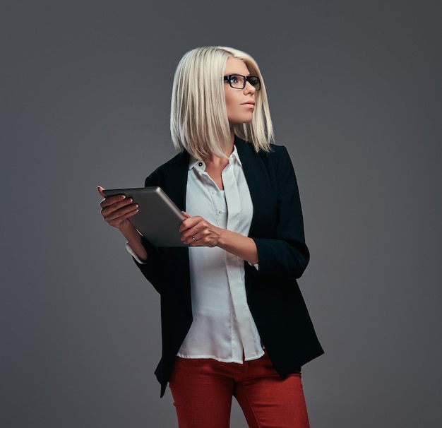 Smart fashionable blogger female in modern clothes and glasses, poses with digital tablet. Isolated on a gray background.