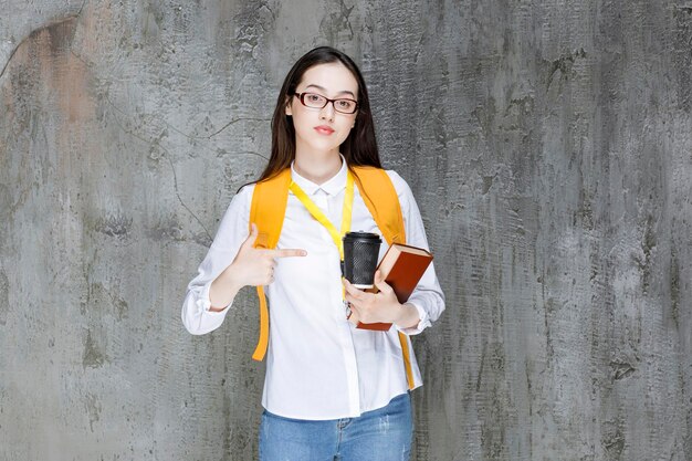 Smart female student in glasses with book and cup of coffee standing. High quality photo