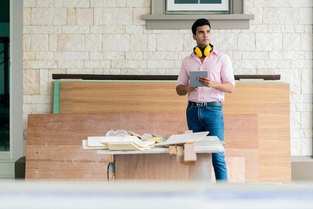 Smart appaltatore falegname indiano con occhiali e cuffie controlla il cornicione del soffitto bianco per il concetto di casa di decorazione d'interni