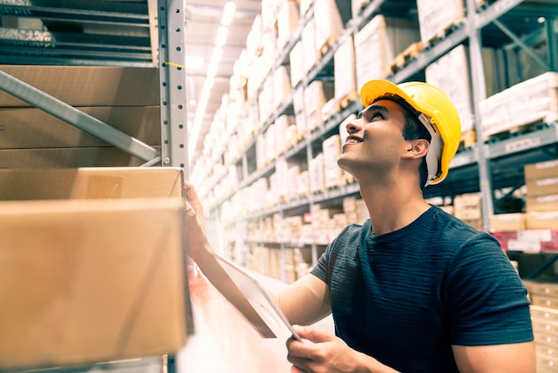 Free photo smart indian engineer man wearing safety helmet doing stock tick check and cardboard stock product management in factory warehouse background