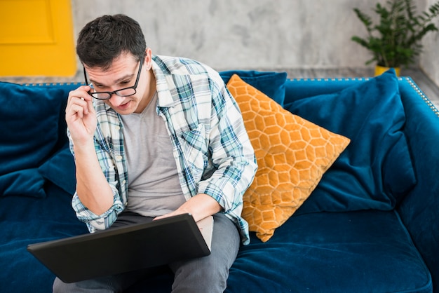 Uomo intelligente che si siede sul divano e guardando portatile