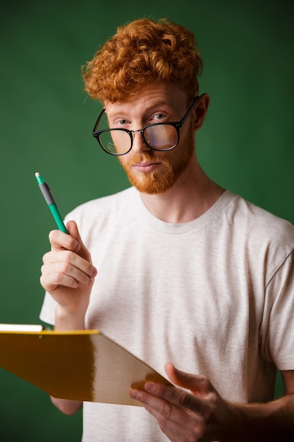 Foto gratuita uomo barbuto di lettura intelligente in tshirt bianca con cartella e penna,