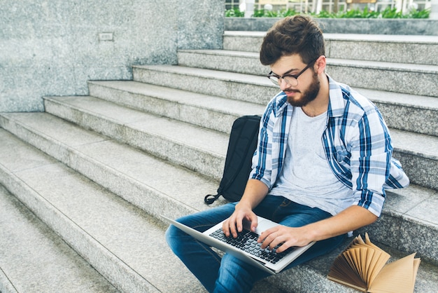 Smart student typing on laptop keyboard resting on the outdoor campus stairs