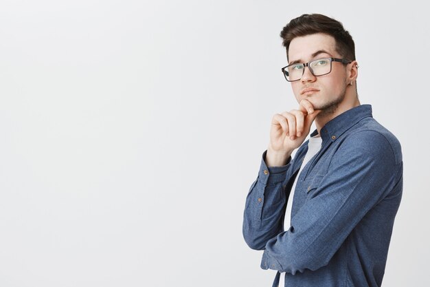 Smart young man in glasses looking thoughtful, pondering idea