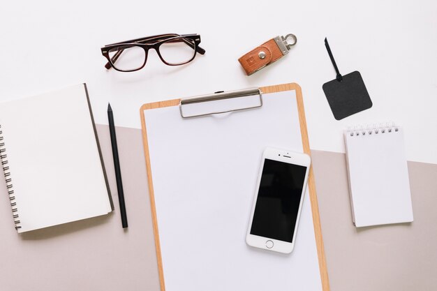 Smartphone on clipboard near glasses and stationery