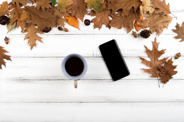 木製の葉の背景にスマートフォンとコーヒーカップ
