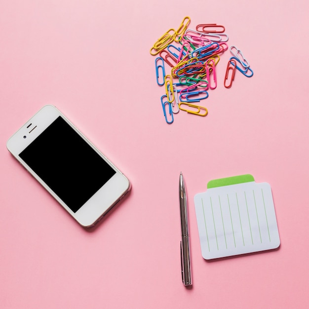 スマートフォン;ピンクの背景にペンとメモ帳とカラフルな紙クリップ