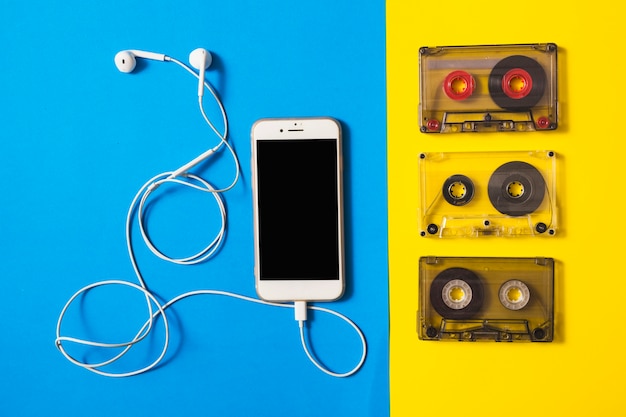Бесплатное фото Смартфон, подключенный к наушникам и кассетным лентам на двойном фоне