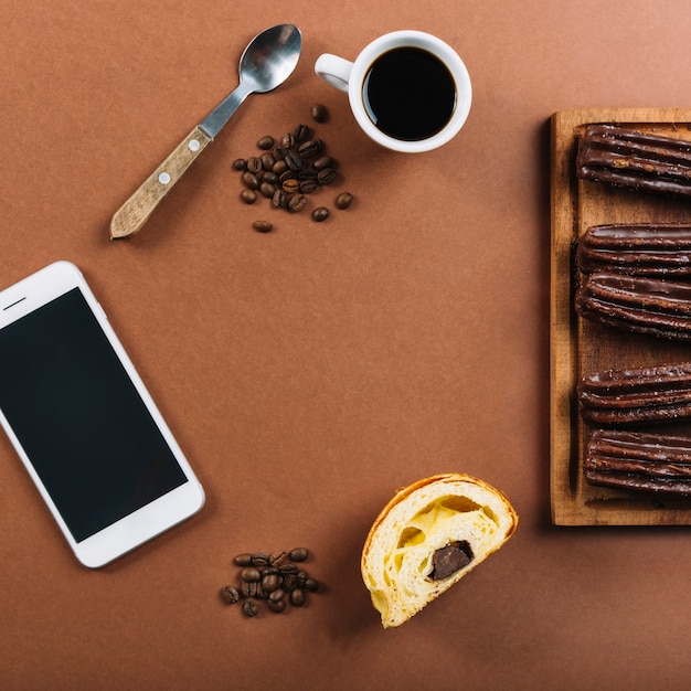 Foto gratuita smartphone, tazza di caffè ed eclairs