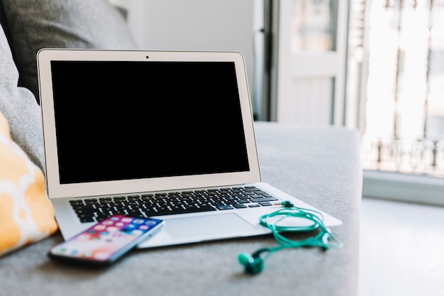 Smartphone and earphones near laptop on sofa