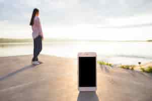 Foto gratuita smartphone di fronte a donna in piedi vicino al lago idilliaco