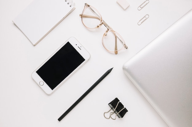 Смартфон и очки возле ноутбука на белом
