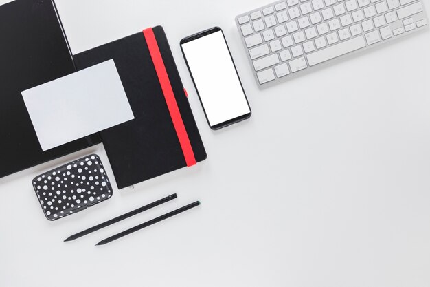 スマートフォンと白いテーブルの上の文房具の近くのキーボード