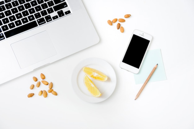 Smartphone; laptop; almond; sweet lime and pencil on white background