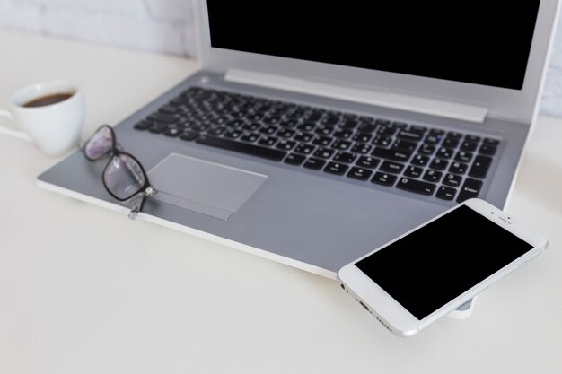 Смартфон на ноутбуке с очками и чашкой кофе
