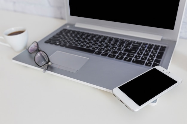 Smartphone on the laptop with spectacles and coffee cup