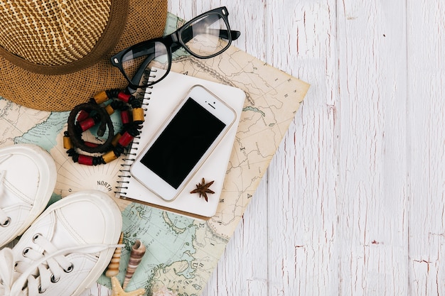Smartphone lies on a notebook beforeon the map, hat, keds and glasses around it