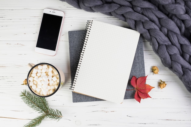 Smartphone near fir branch, cup with marshmallows and notebook