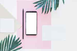 Free photo smartphone near papers and palm trees on white desk