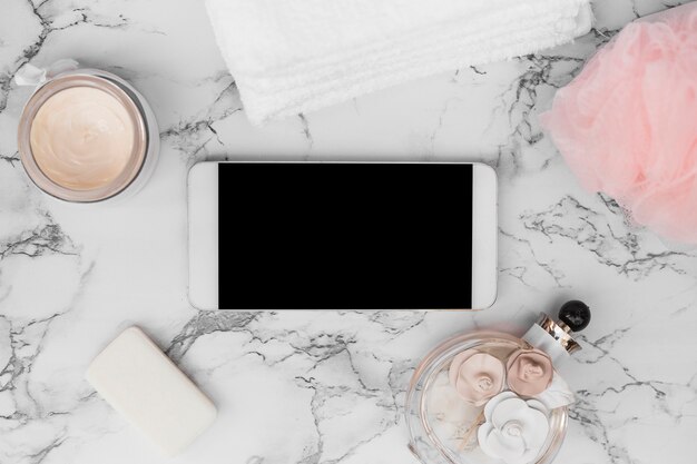 Smartphone; perfume bottle; towel; soap; moisturizing cream and loofah on marble background