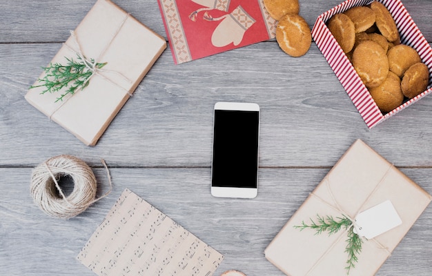 Smartphone between presents, cookies in box, post cards and bobbin of thread