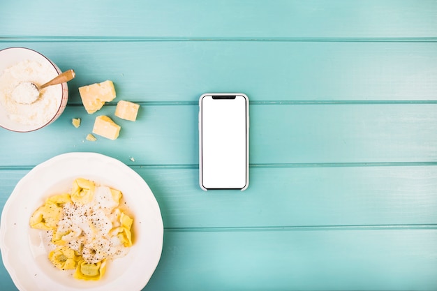 Foto gratuita smartphone con schermo bianco vuoto oltre al piatto di pasta