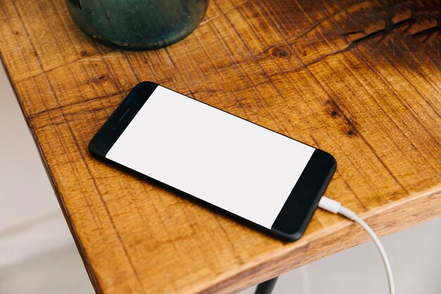 Smartphone with blank white screen on wooden desk