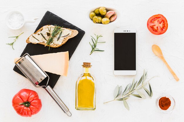 Smartphone with cheese, bread and ingredients on white backdrop