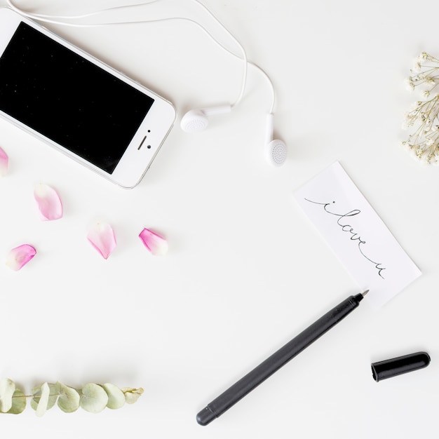 Smartphone with earphones near tag with title, pen, fresh rose petals and plant twigs