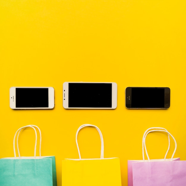 Smartphones with shopping bags on yellow table