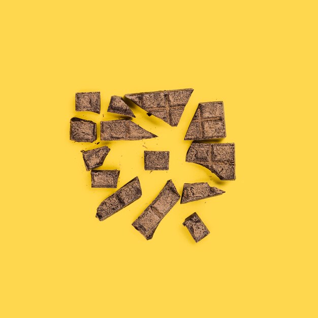 Разбитые кусочки шоколада на желтой поверхности